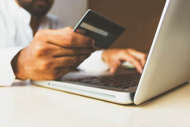 a man having a credit card in front of a laptop